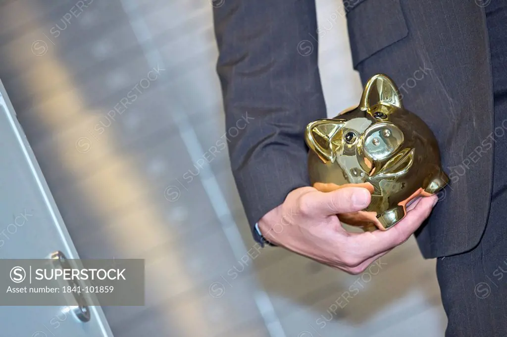 Man in front of safe deposit boxes holding golden piggy bank, close_up