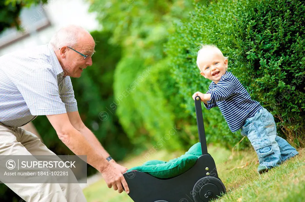 Grandfather and toddler with doll´s pram outdoors