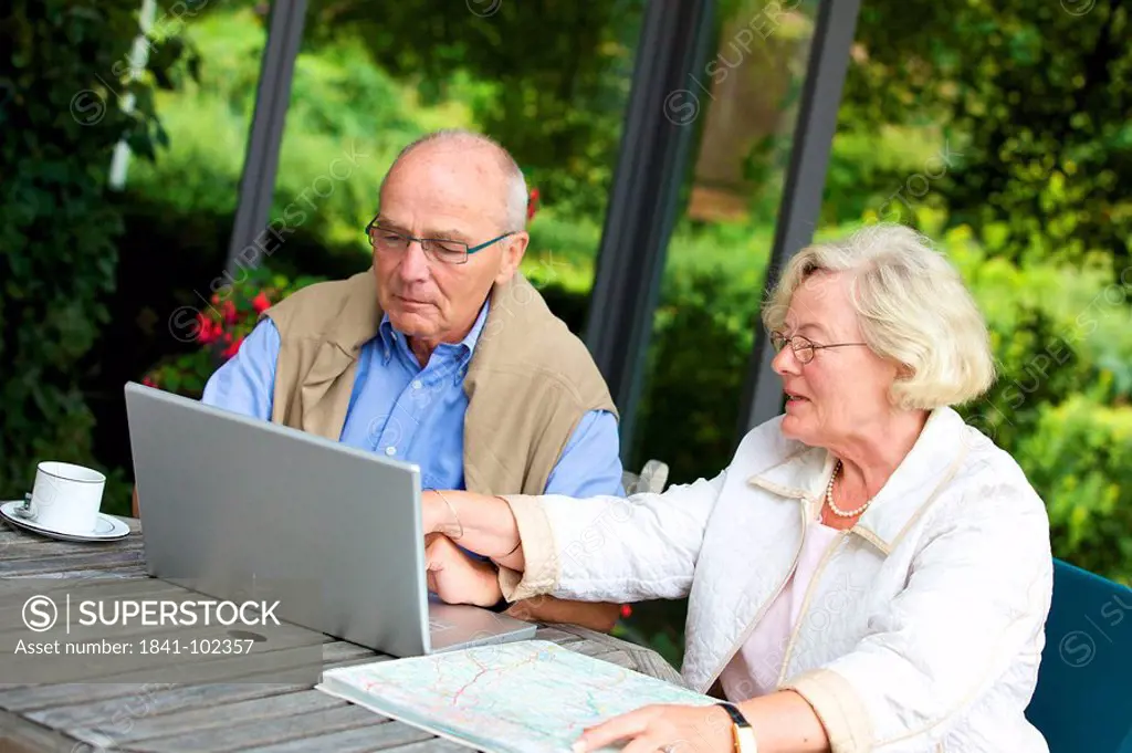 Senior couple on terrace with laptop and road map