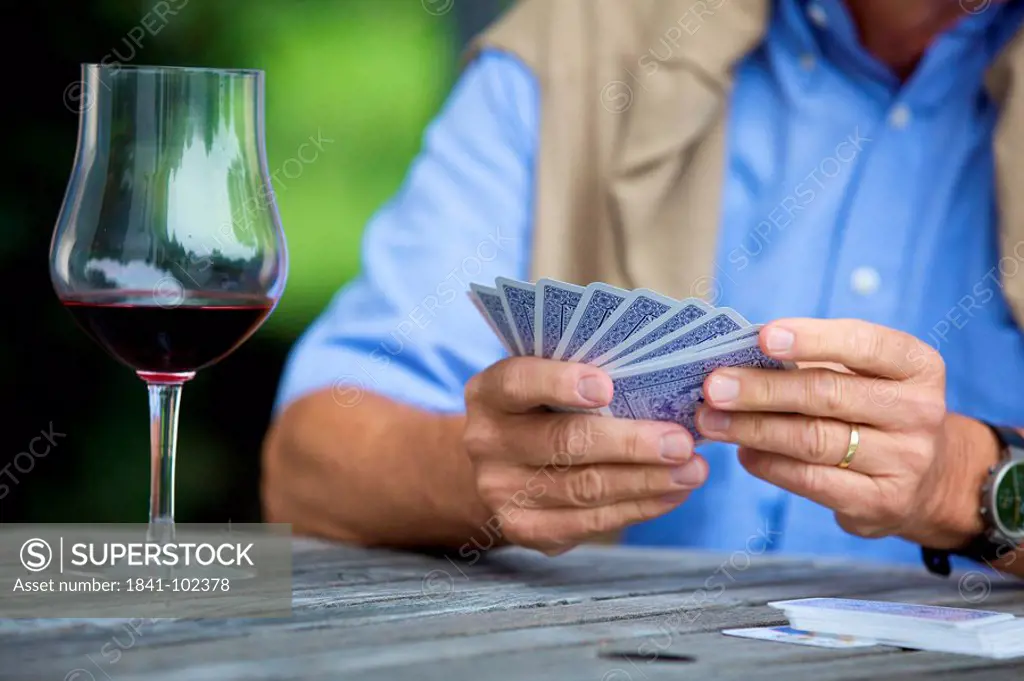 Senior man playing cards and drinking red wine, close_up