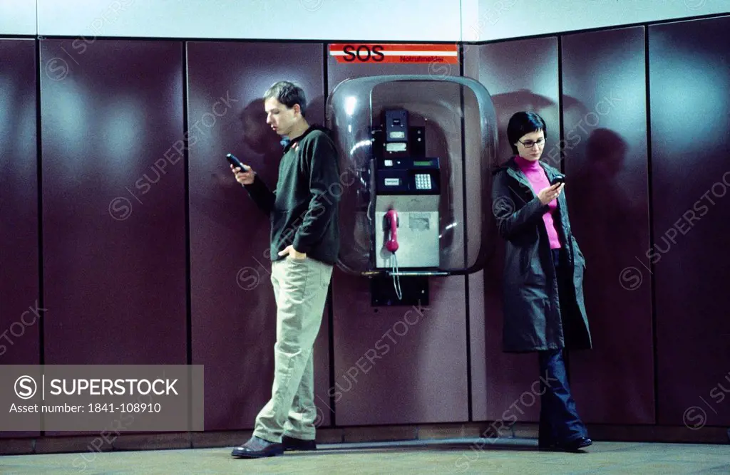 Young couple using mobile phones against telephone booth