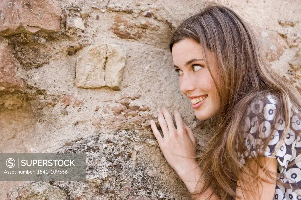Smiling young woman with long brown hair at stone wall