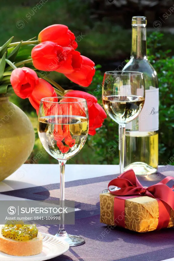 White wine, gift and bunch of tulips on garden table