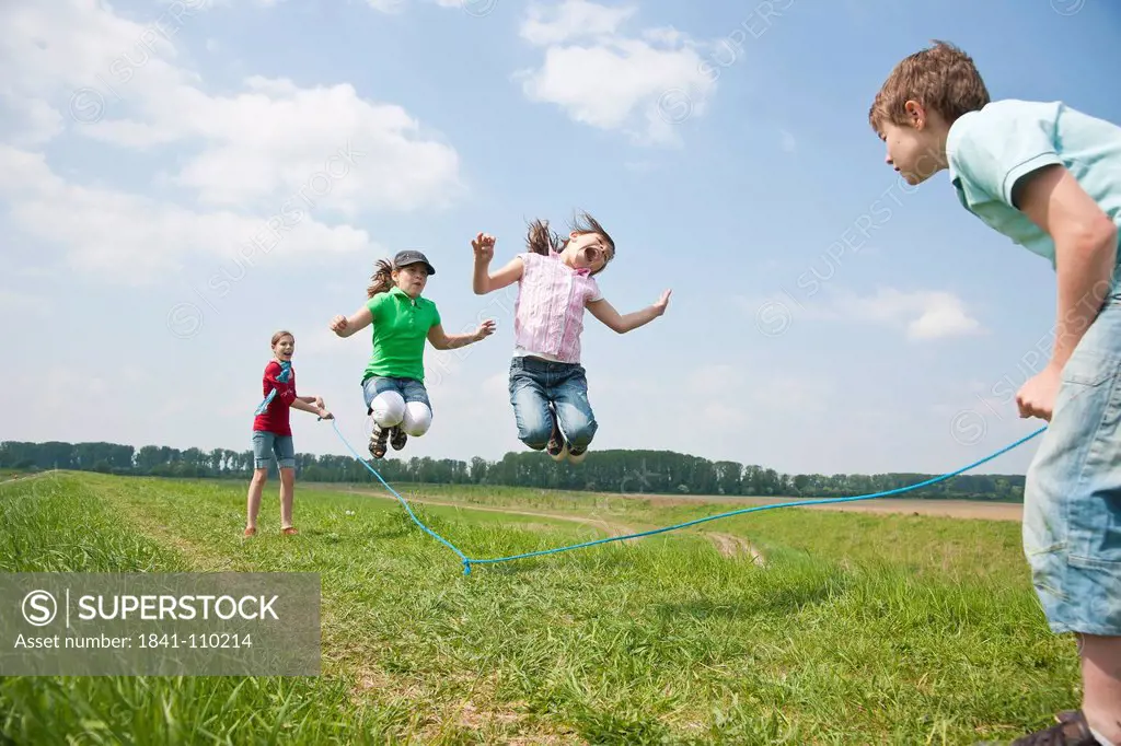 Four children skipping rope in meadow