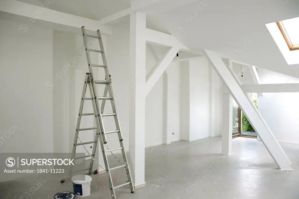 Ladder and paint bucket in an empty attic flat