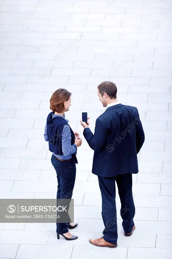 Businessman and businesswoman standing with cell phone outdoors