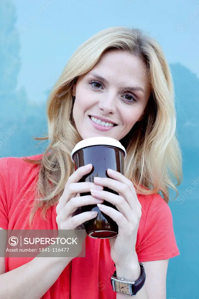 Smiling blond woman holding coffee to go