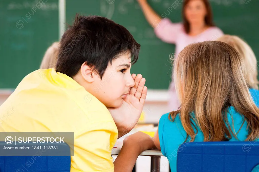 Boy whispering to girl in classroom