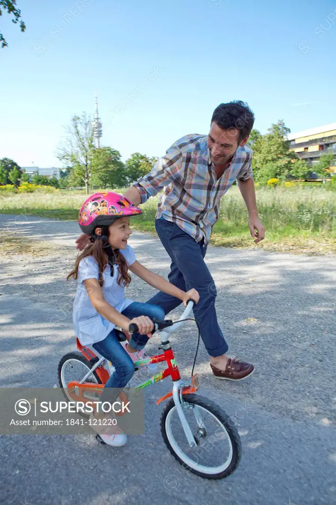 Father running next to daughter on bike