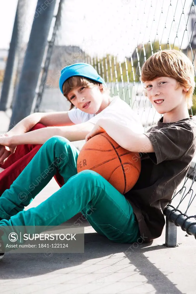 Two boys sitting with basketball at fence