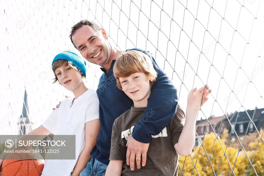 Father and two sons with basketball on sports ground