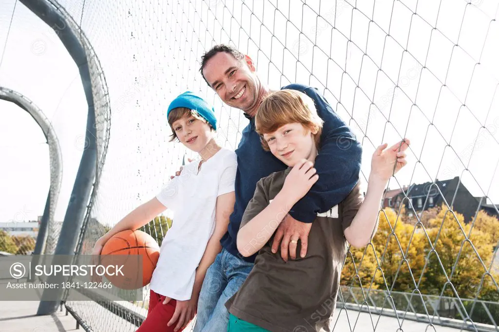 Father and two sons with basketball on sports ground