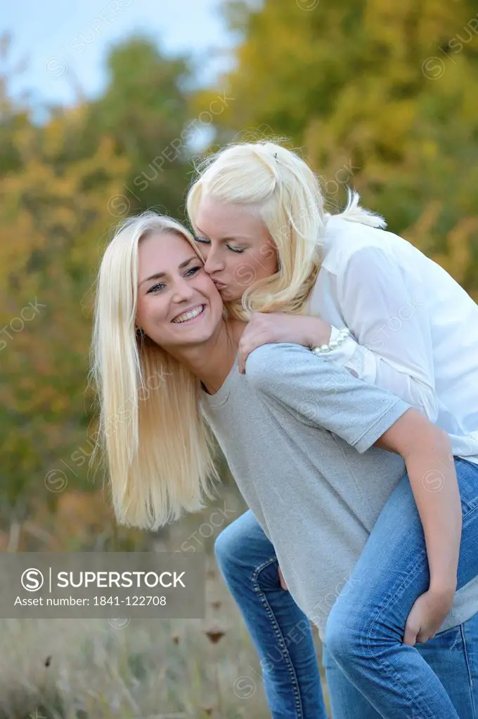 Happy young blond woman carrying her friend piggyback