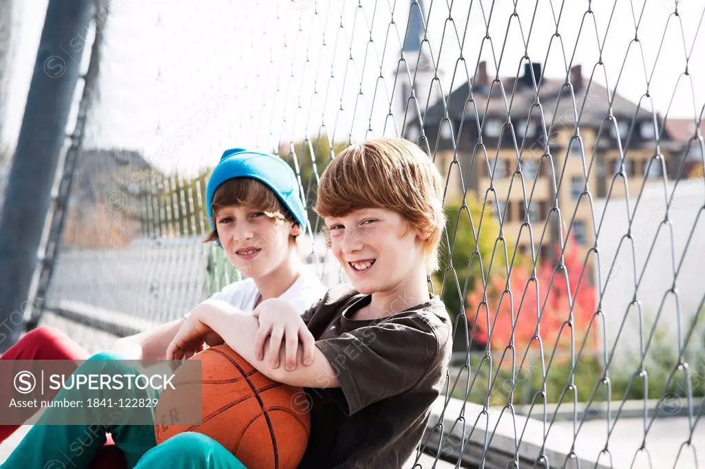 Two boys sitting with basketball at fence