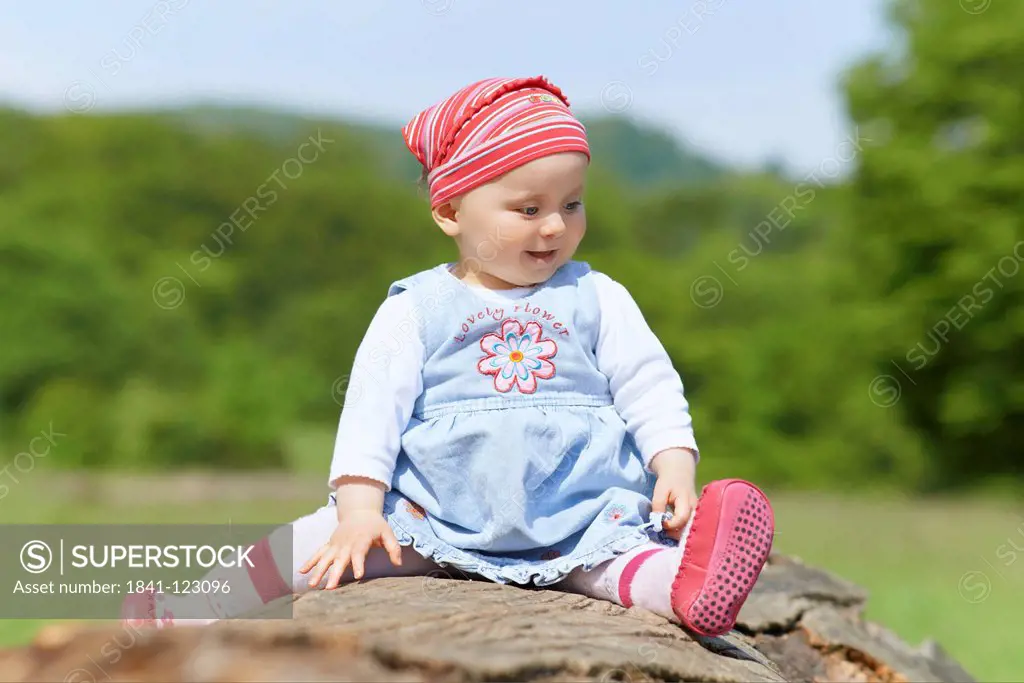 Happy female baby sitting on tree stump