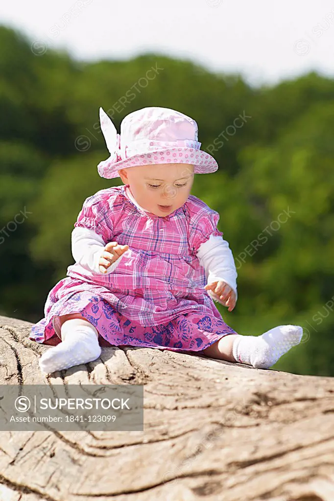Female baby sitting on tree stump