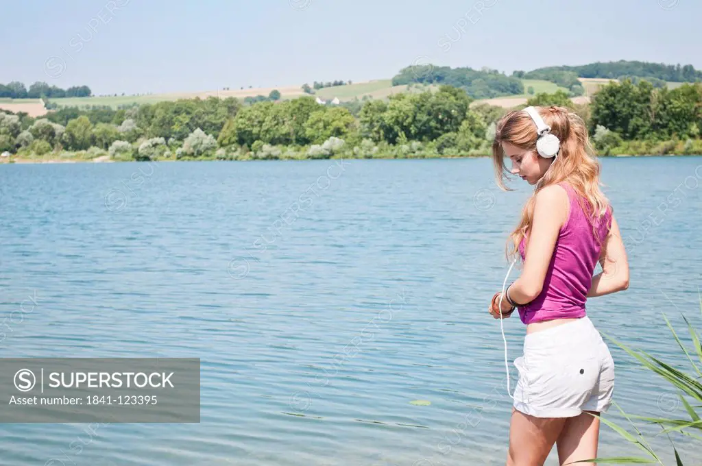 Serious young woman listening to music at a lake