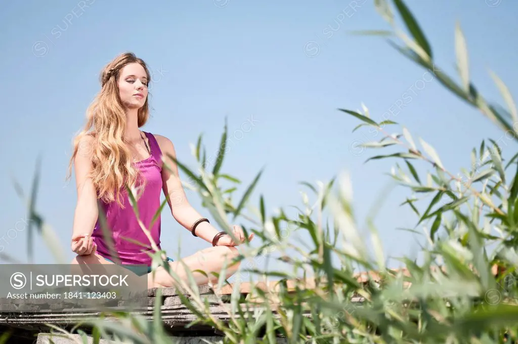 Blond young woman practicing yoga at a lake