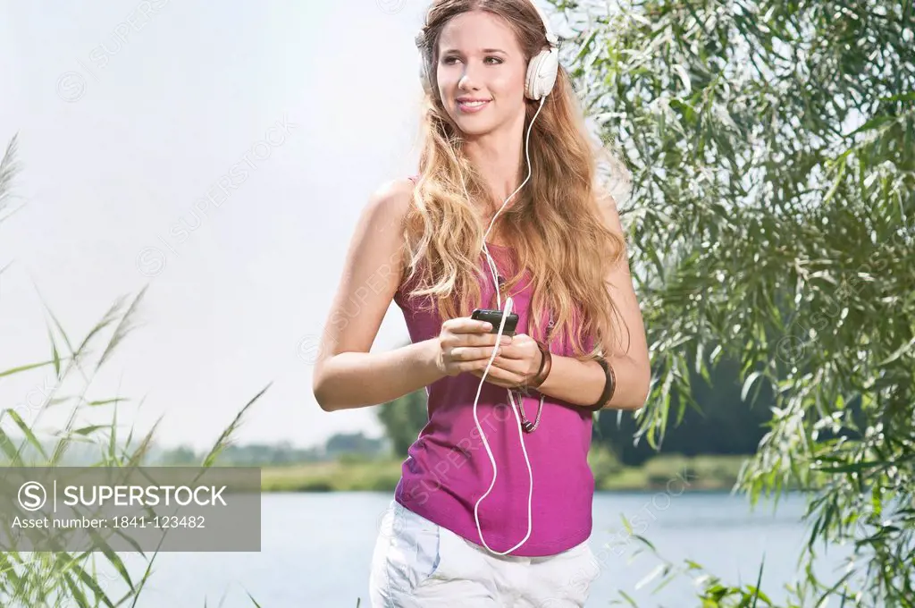 Blond young woman listening to music at a lake