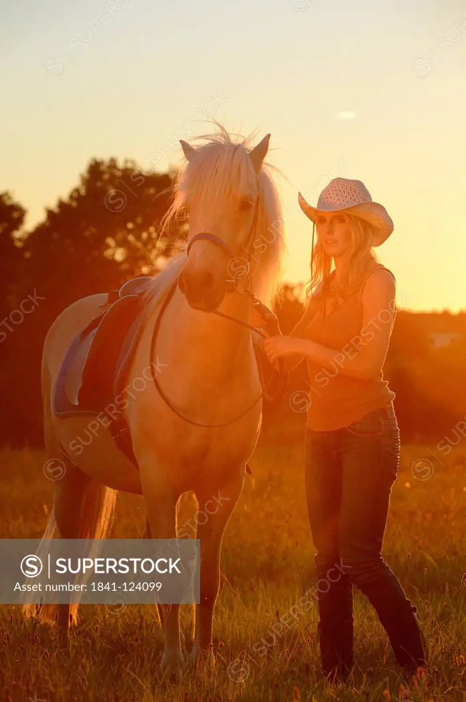 Young woman with horse on meadow in backlight