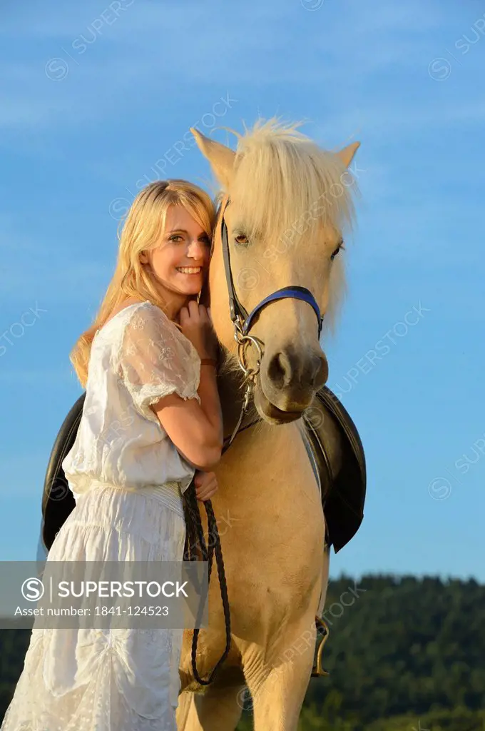 Smiling woman in white dress with horse under blue sky