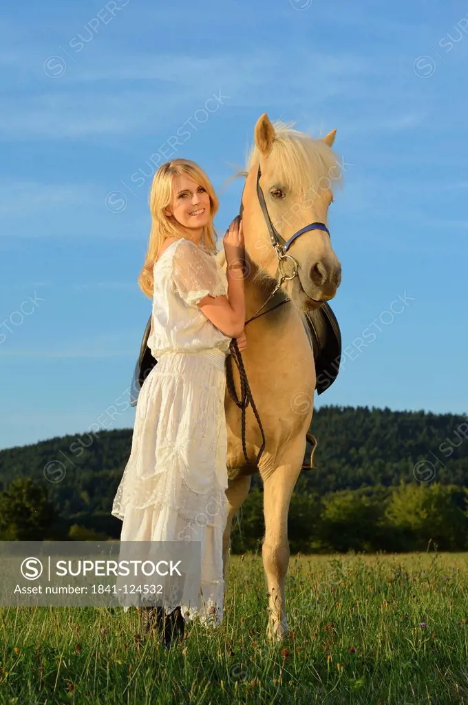 Smiling woman in white dress with horse on meadow