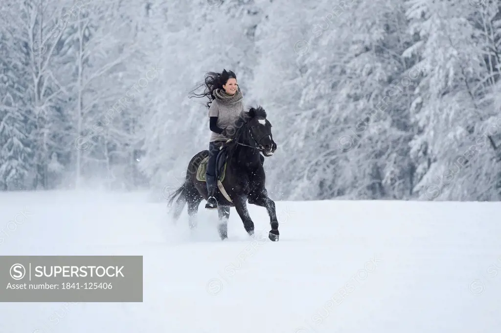Young woman riding on horse in snow