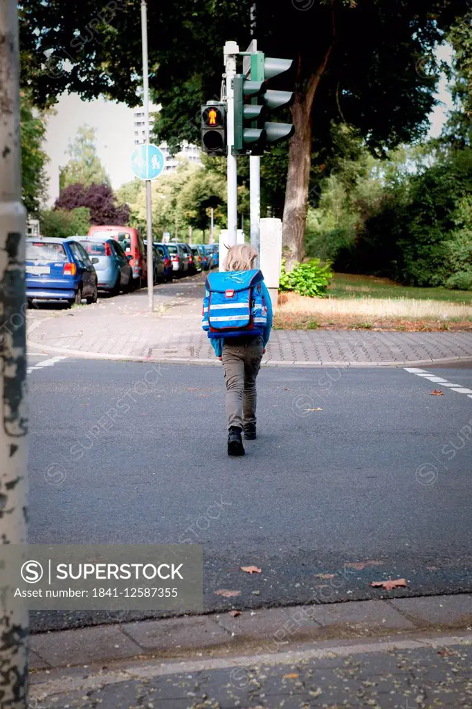 A girl on her way to school is crossing the road when the traffic light shows red.