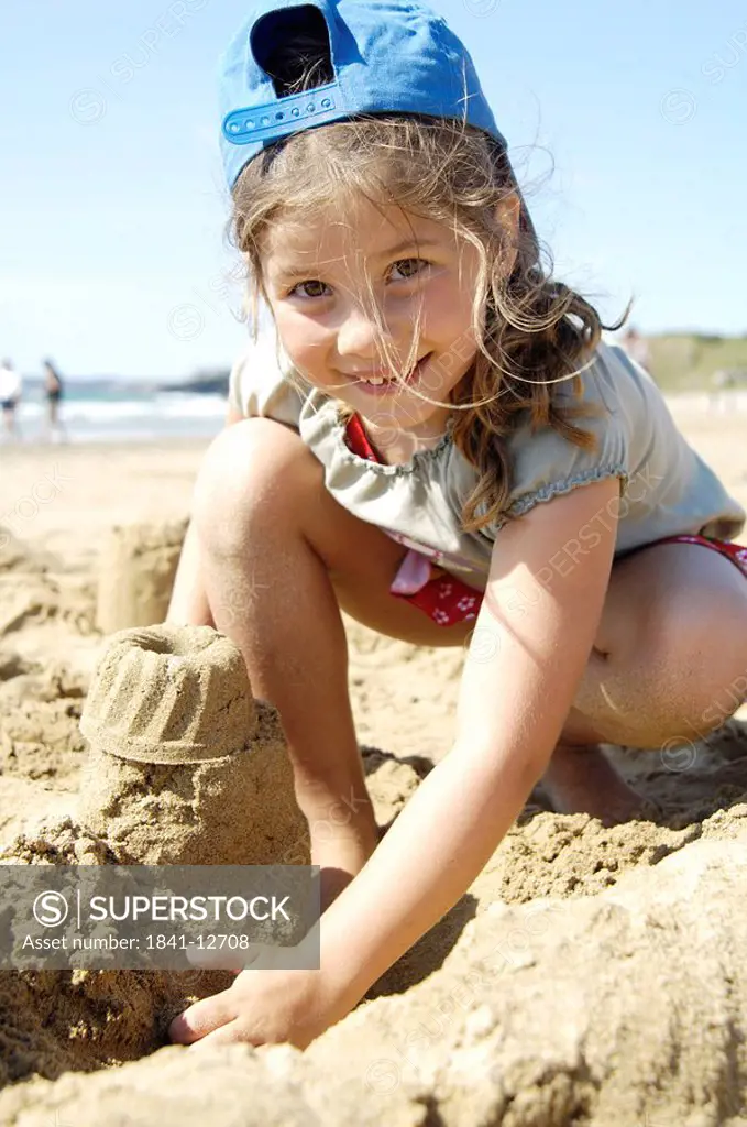 Portrait of girl making sandcastle on beach and smiling