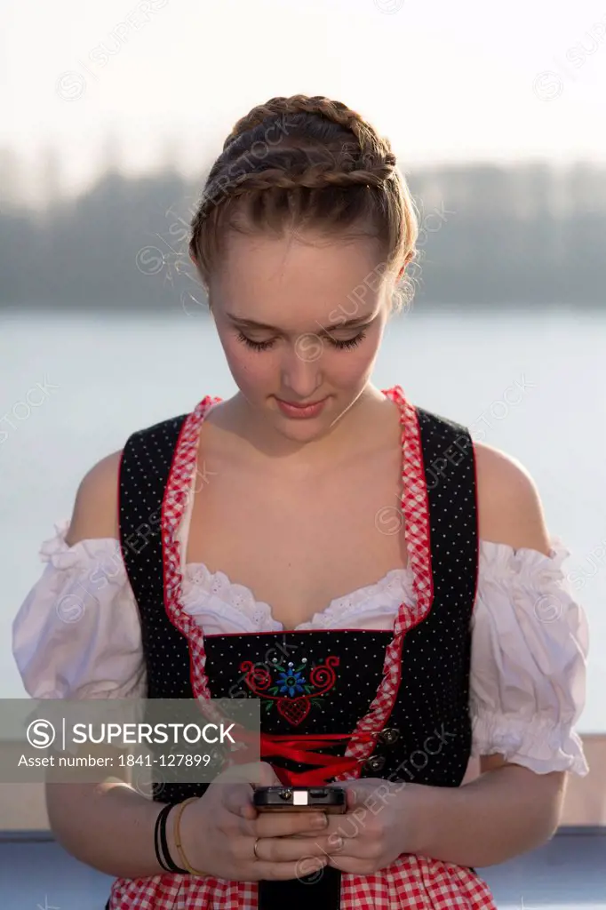 Teenage girl wearing dirndl with mobile phone, Lichtenau, Baden-Wuerttemberg, Germany, Europe