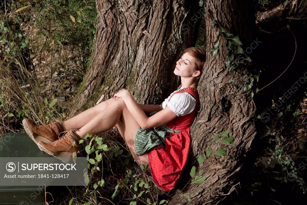 Woman in dirndl sitting at tree