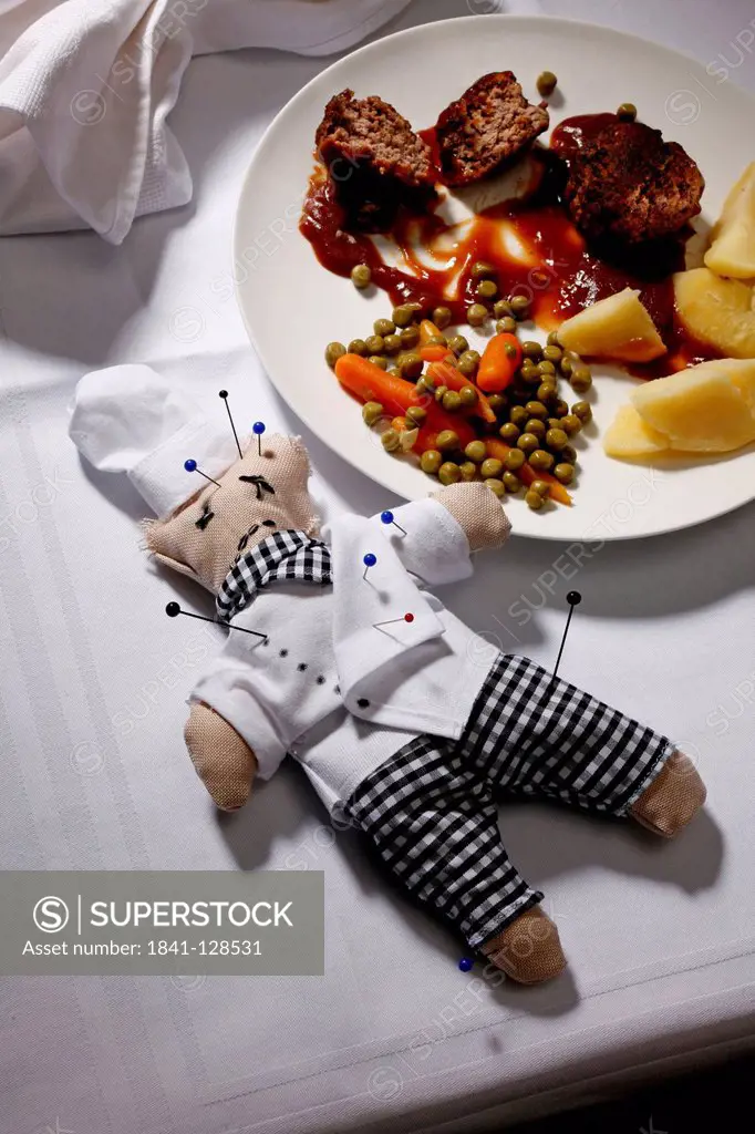 Voodoo doll of a cook with pins on laid table next to dish