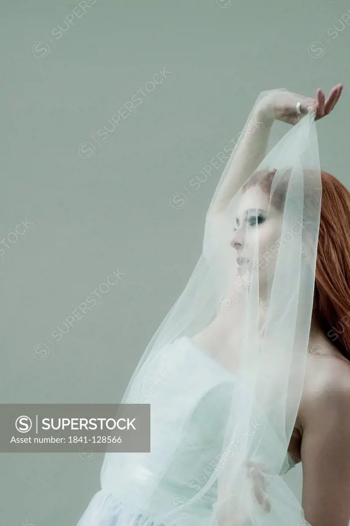 Red-haired young woman wearing dress and transparent cloth