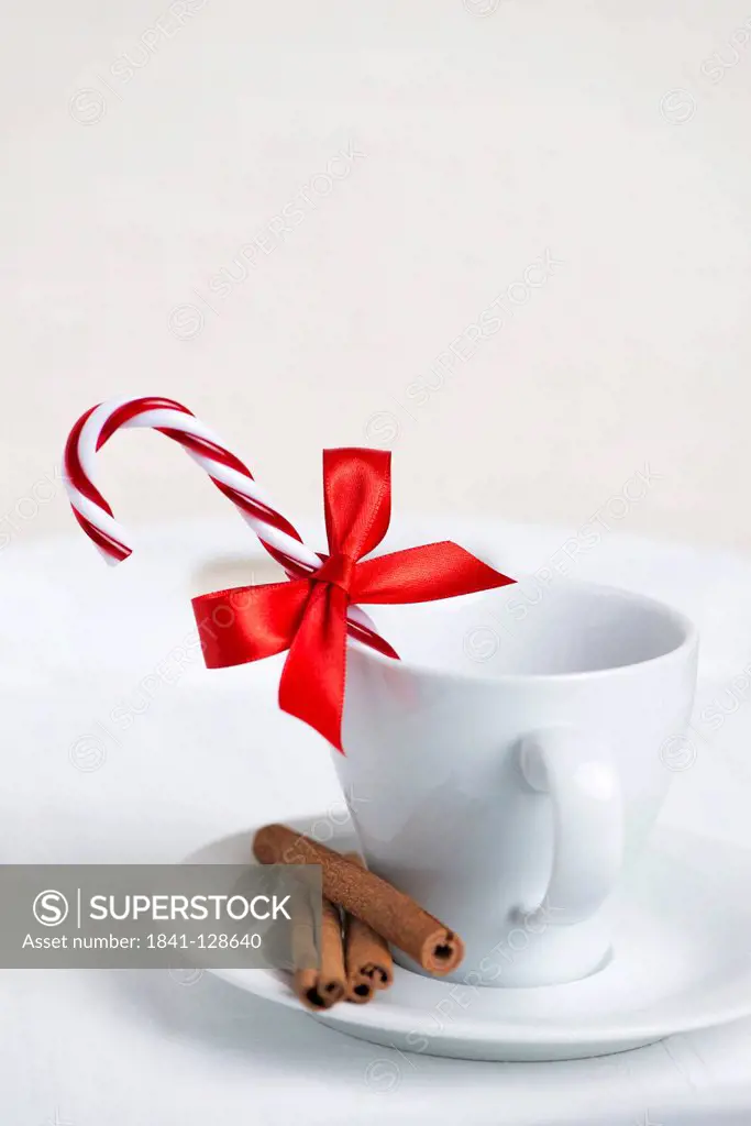 Cup decorated with candy cane, red ribbon and cinnamon sticks