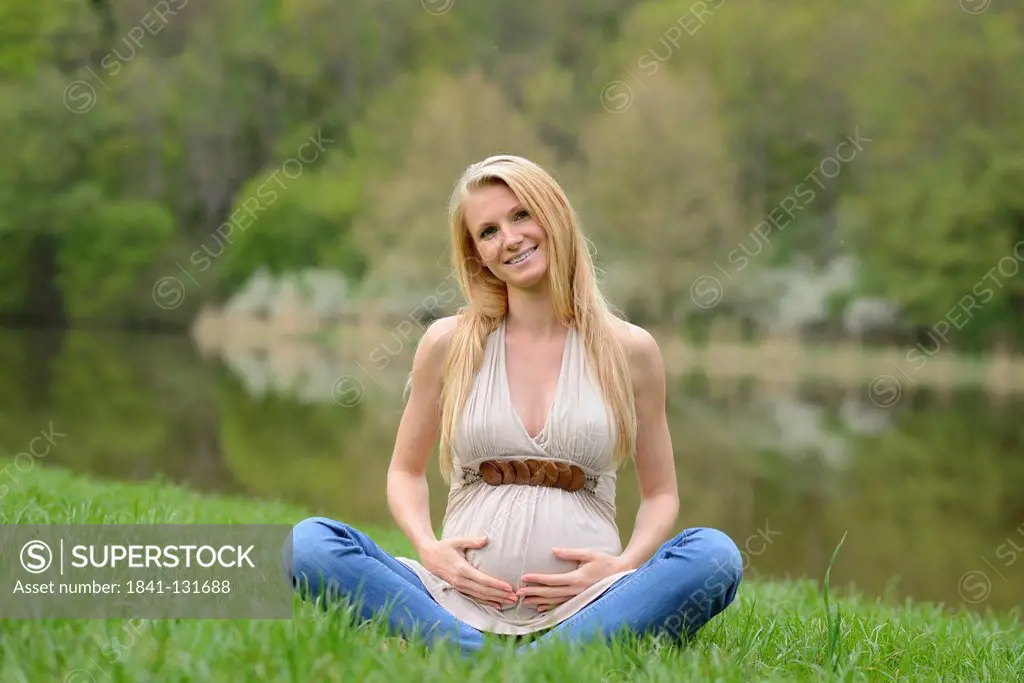 Headline: Young pregnant woman sitting on a meadow