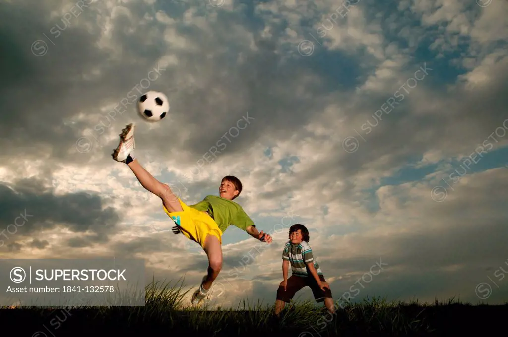 Two boys are playing football in a meadow.