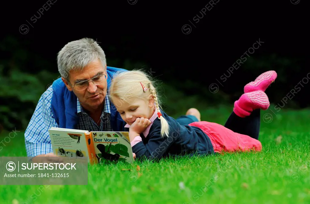 Grandfather and granddaughter are reading in the garden.