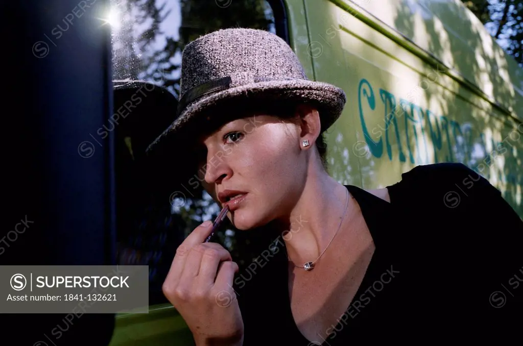 Woman with Hat is Putting on Lip Gloss.