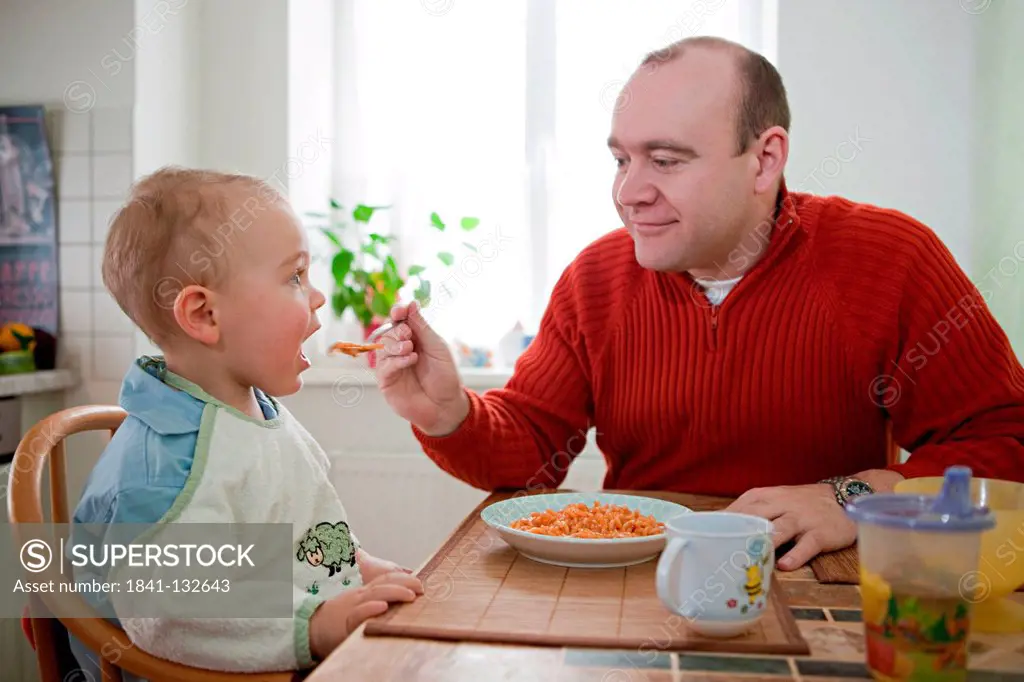 A father is feeding his son.