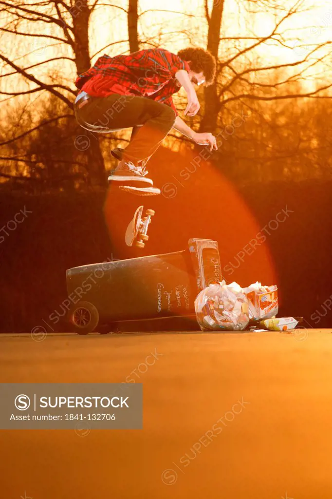 Skateboarder performing a trick jumping over a garbage can.