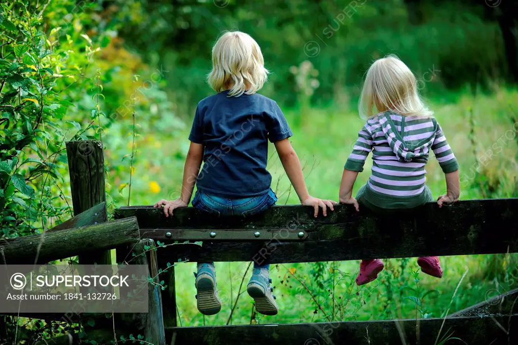 Boy and girl are sitting on a fence.
