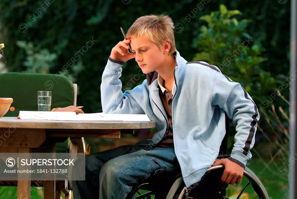Boy in a wheelchair is doing his homework.