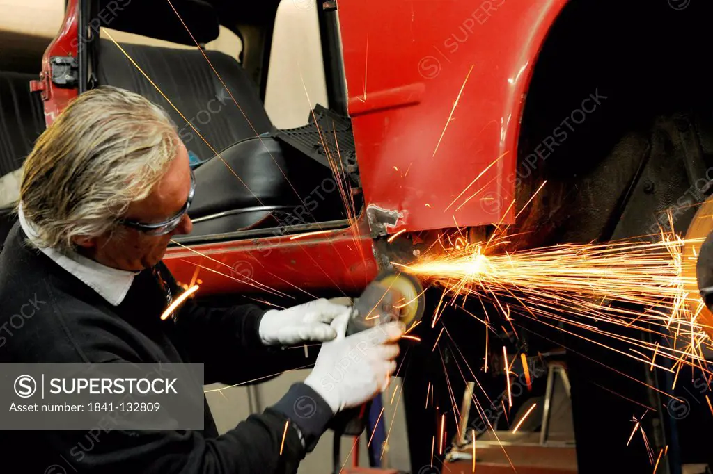 A car mechanic is grinding off rust from a car.