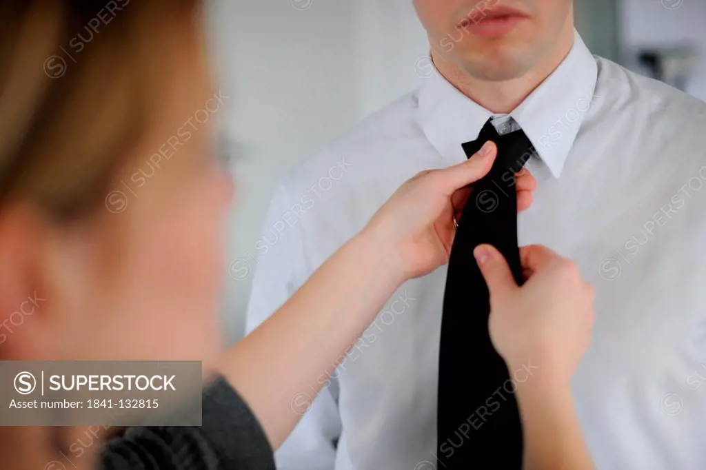 A woman is knotting the tie of a businessman.
