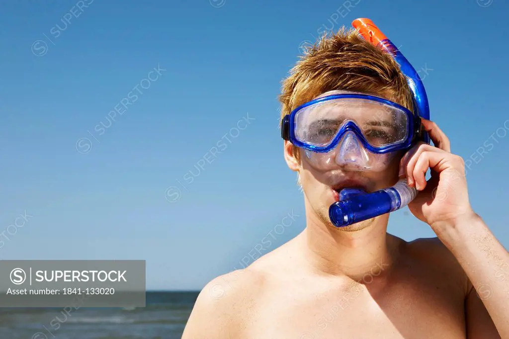 Portrait of a young blonde man with snorkel and diving goggles standing at the sea.