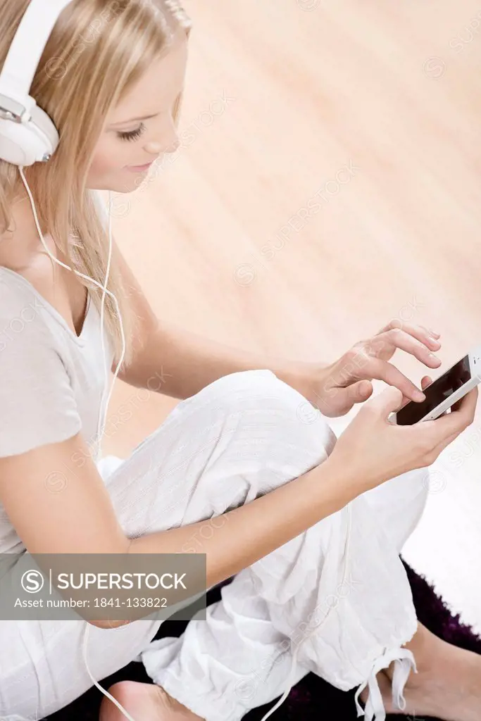 Young blond woman with smartphone and headphones at home