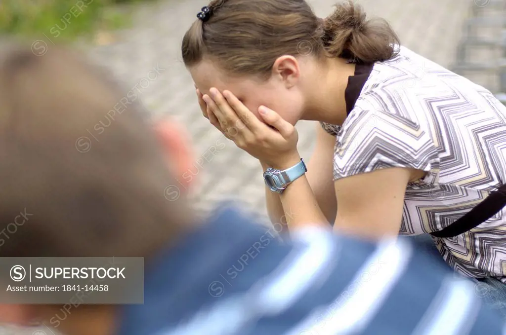 Side profile of teenage girl sobbing with her friend sitting beside her