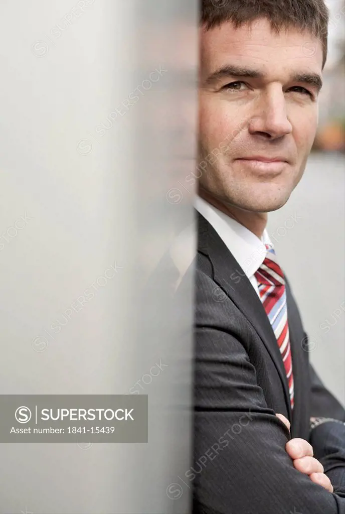 Businessman leaning against wall, eye contact