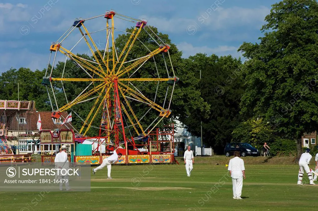 People playing cricket with ferris wheel in field, England