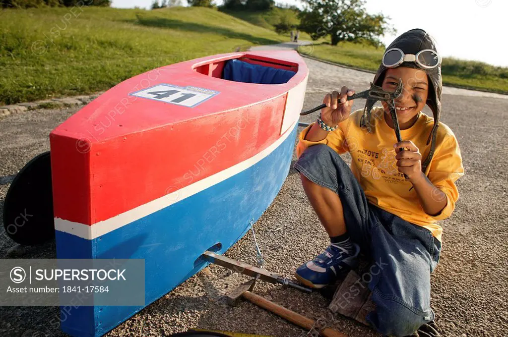 Portrait of boy repairing soapbox and smiling